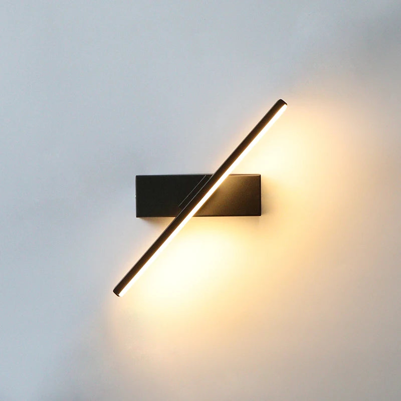 Arc 330-degree adjustable LED bedside wall lamp in black aluminium beside a bed with open book