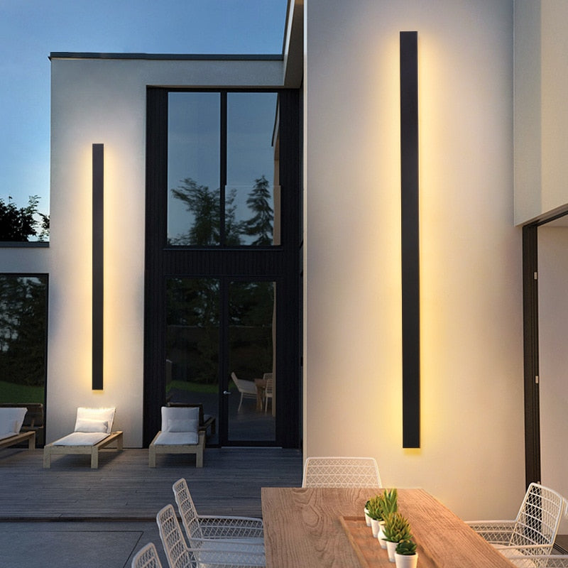 Funkis frosted black aluminium outdoor wall light mounted on a garden wall at night