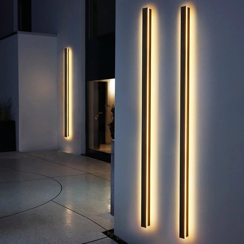 Funkis frosted black aluminium outdoor wall light mounted on a garden wall at night