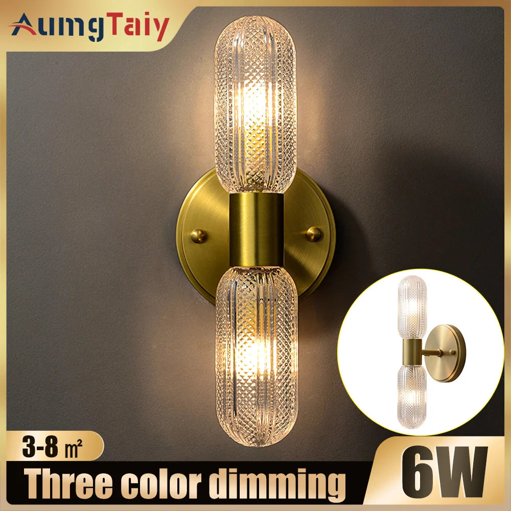 Harlow gold glass wall sconce with copper arm mounted in a living room beside an armchair