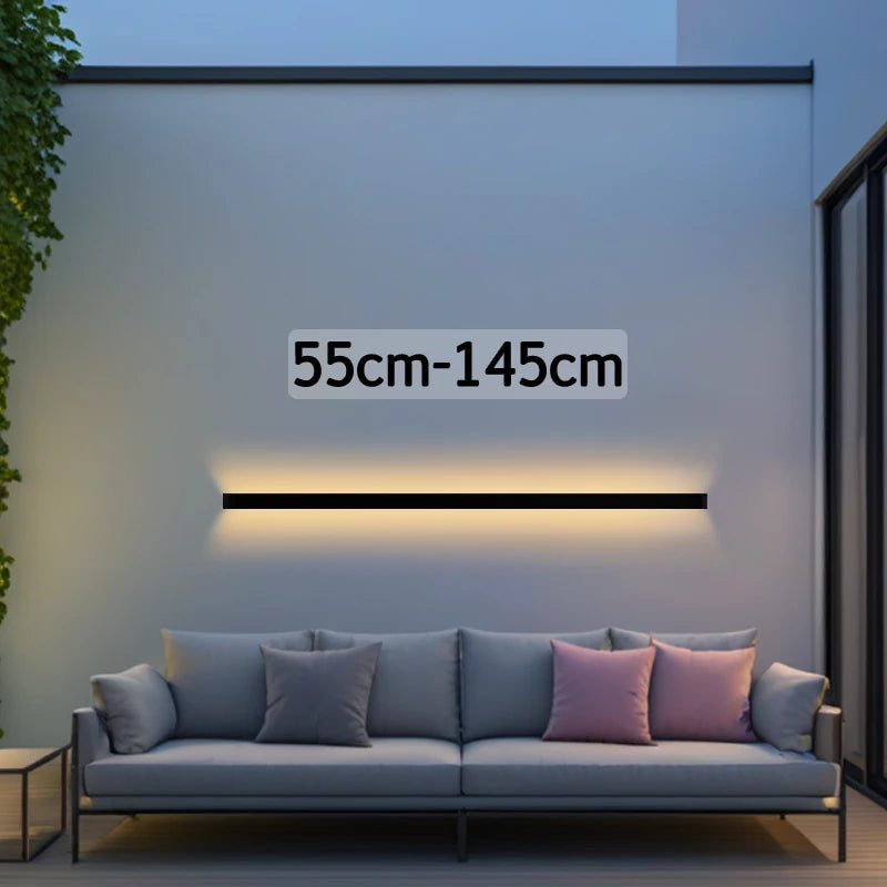Croft linear LED wall sconce mounted vertically beside a bedroom headboard, casting a warm wash of light