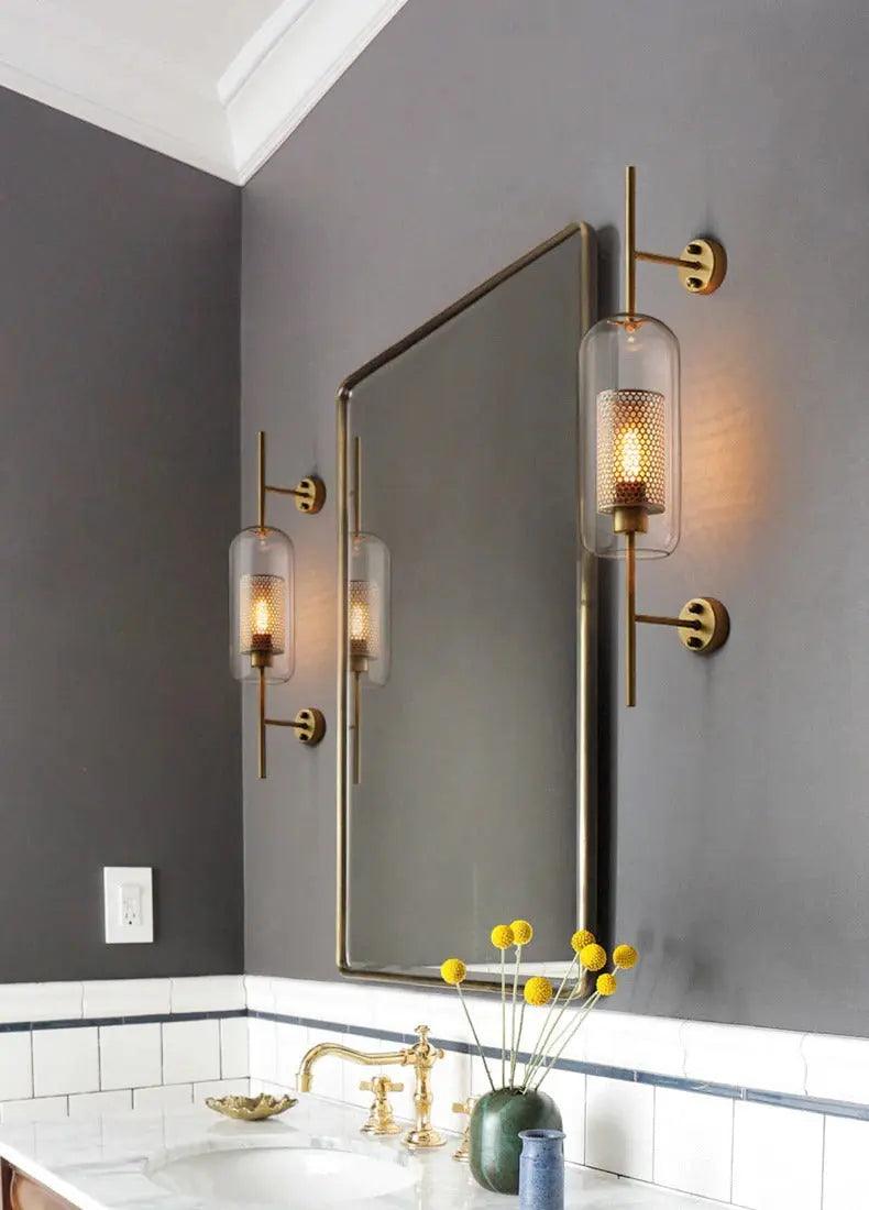 Alegria gold glass wall sconce flanking a bathroom mirror, casting warm light