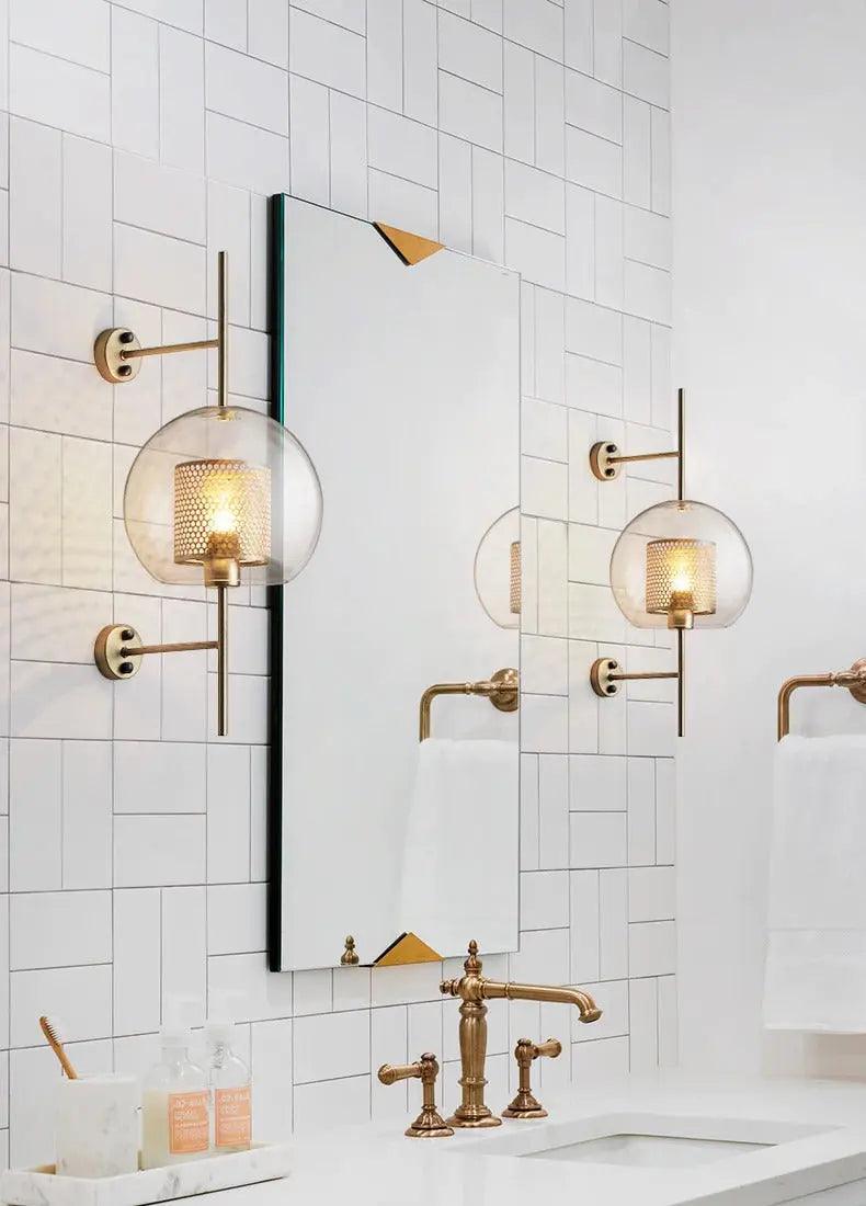 Alegria gold glass wall sconce flanking a bathroom mirror, casting warm light