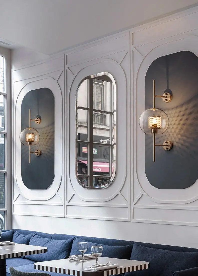 Alegria gold glass wall sconce flanking a bathroom mirror, casting warm light
