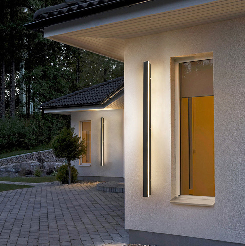 Funkis frosted black aluminium outdoor wall light mounted on a garden wall at night