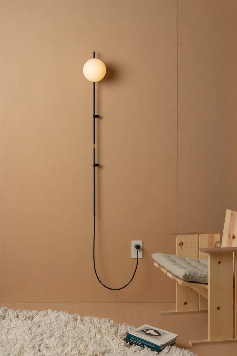 Sol Nordic plug-in wall sconce in black mounted in a living room beside a sofa