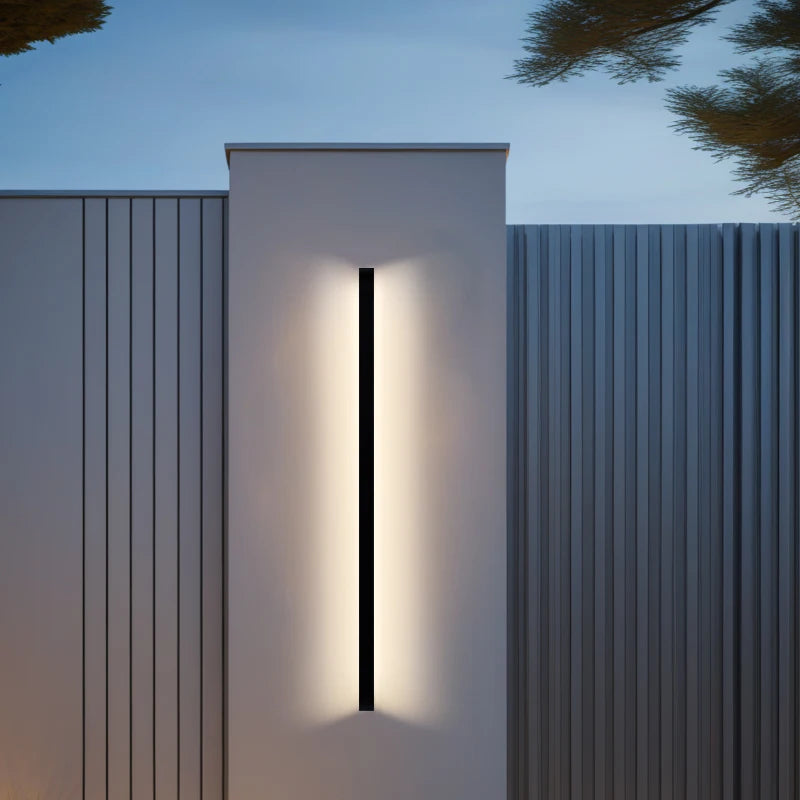 Croft linear LED wall sconce mounted vertically beside a bedroom headboard, casting a warm wash of light