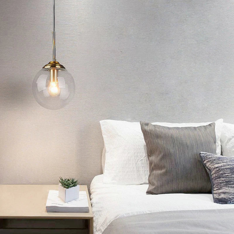 Orla amber glass and metal pendant light hanging above a bedside table in a Nordic-style bedroom
