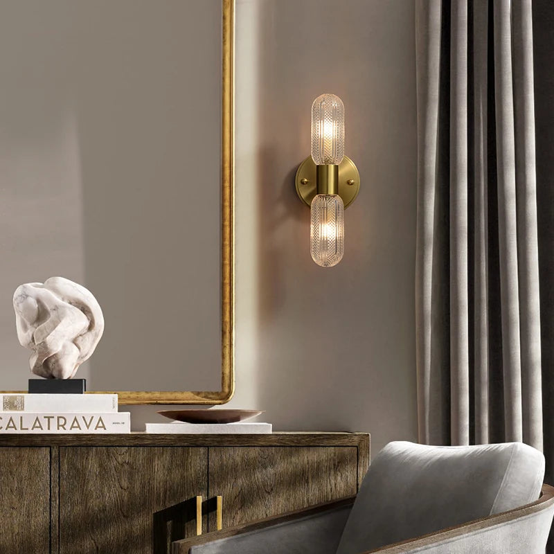 Harlow gold glass wall sconce with copper arm mounted in a living room beside an armchair